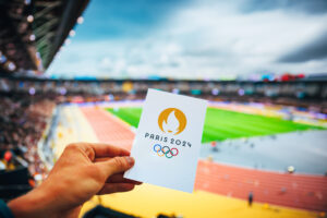 PARIS, FRANCE, JANUARY. 17. 2024: Paris 2024 Summer olympics games, man holding in hand ticket for track and field event at paris 2024 olympics. Modern Athletics olympics Stadium in background